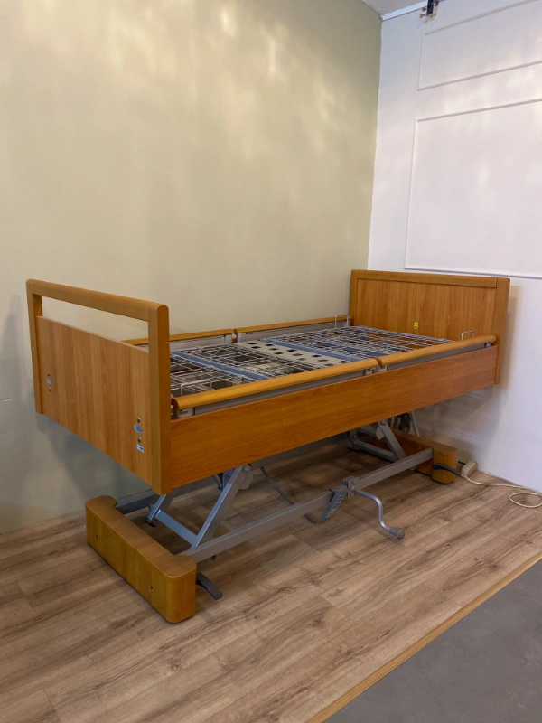 Fa borítású elektromos ápolási ágy emelt pozícióban, rácsos fekvőfelülettel.